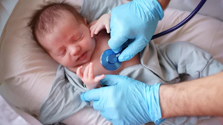 Male in blue medical gloves uses a stethoscope as he listens closely to a baby